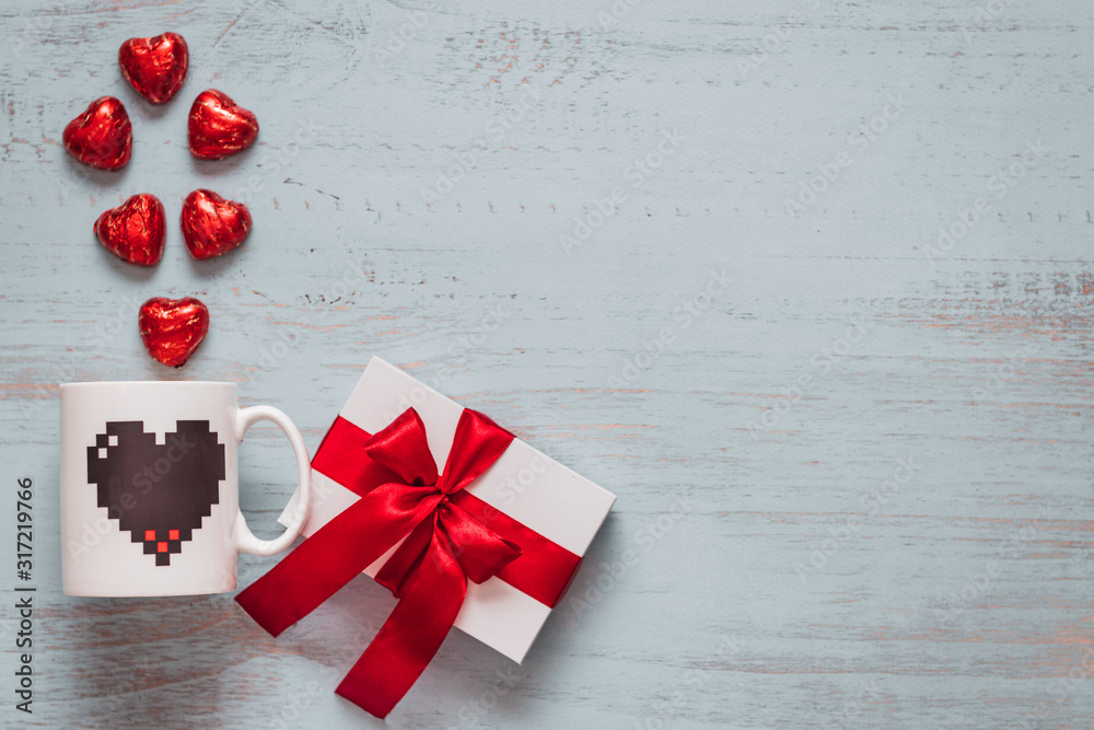 Chocolate hearts, mug and a white present with red ribbon on a light painted wooden background. Top side angle view, flat lay. Valentines day concept. Copyspace. Chocolate hearts, mug and a white present with red ribbon on a light painted wooden background. Top side angle view, flat lay. Valentines day concept. Copyspace.