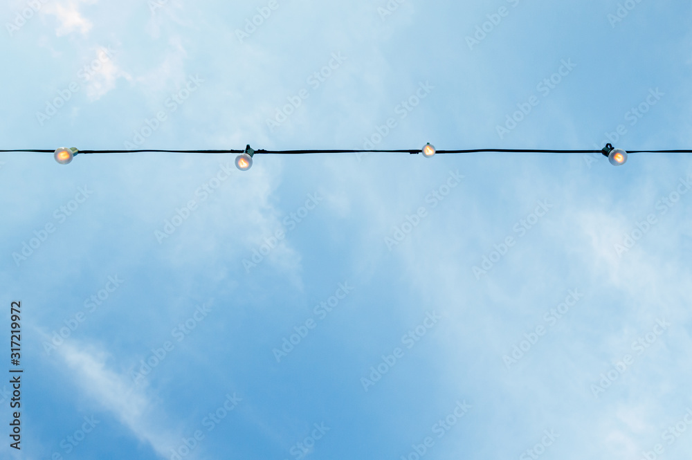 A string of light bulbs hanging in the blue sky. Background