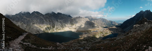 Scenic view of the Tatra Mountains on a sunny summer day, with green valleys, rugged peaks, and a cloudy blue sky.