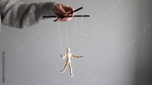Manipulator female hand manipulates a wooden doll on a gray background. Management or suppression concept photo