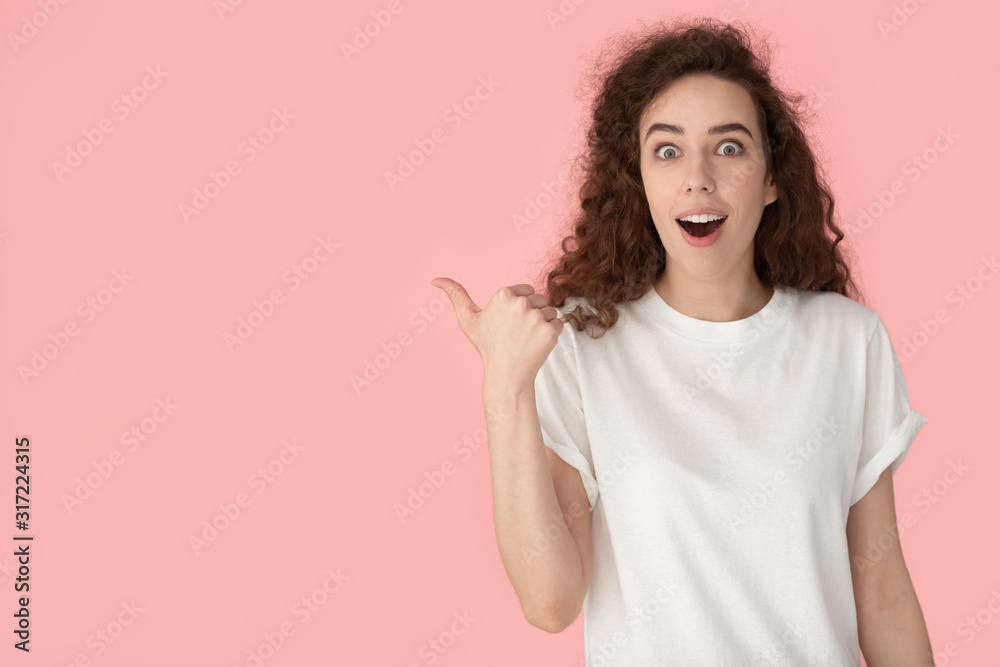 Surprised young woman in white blank t-shirt pointing finger aside.