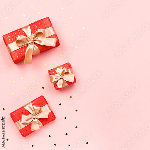Creative Valentine's Day greeting card with red decorations and gift boxes, golden heart confetti on pink background, copy space, top view