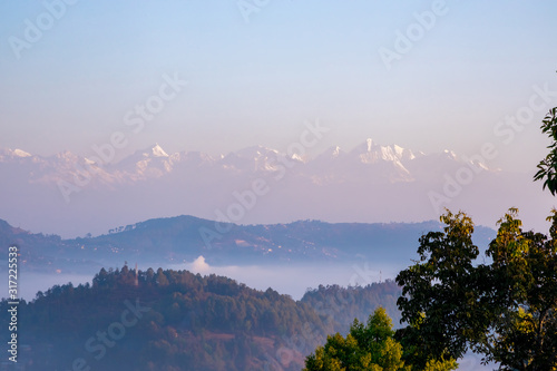 Moody Dramatic view of hills covered in fog and Great Himalaya Range in the backdrop. Terrace farming