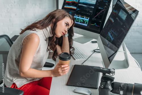 displeased art editor holding paper cup and looking at computer monitor