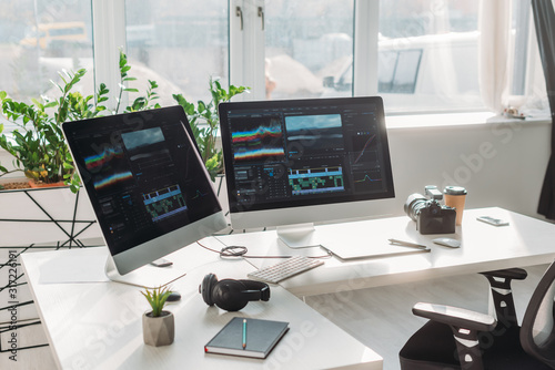 computer monitors with storyboard near headphones and paper cup on table photo