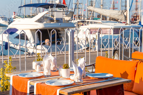 Summer cafe with bright orange tables by the sea on a sunny day with a view of the yachts and palm trees