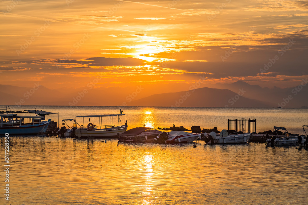 Early morning sunrise view of fisherman boats in Halikiopoulou lagoon. Kanoni, Corfu island, Greece on background of rising sun.