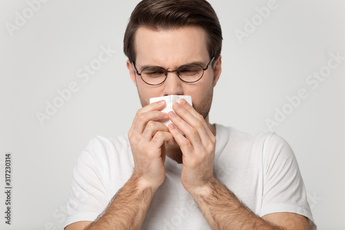Fototapeta Naklejka Na Ścianę i Meble -  Sick millennial guy caught cold, sneezing, feeling unwell.