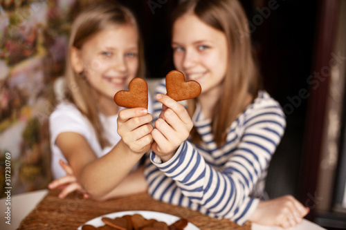 Charming  funny and laughing girls on a blurry background are holding heart-shaped cookies on an outstretched arm  two hearts  close-up