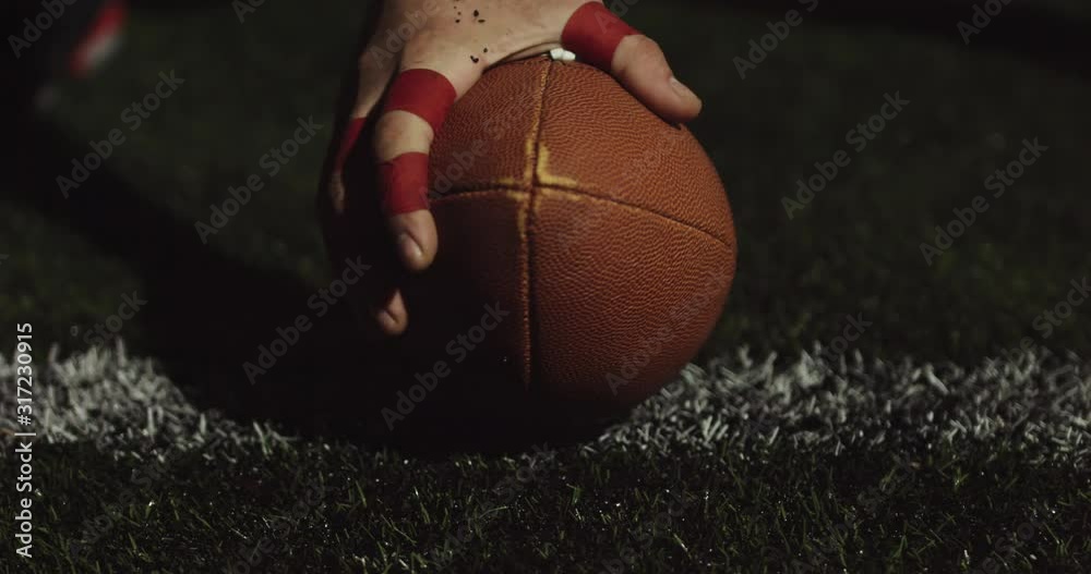 EXTREME CU of Caucasian male American football player holding a ball on grass to start game. Slow motion 60 fps 4K RAW edit footage