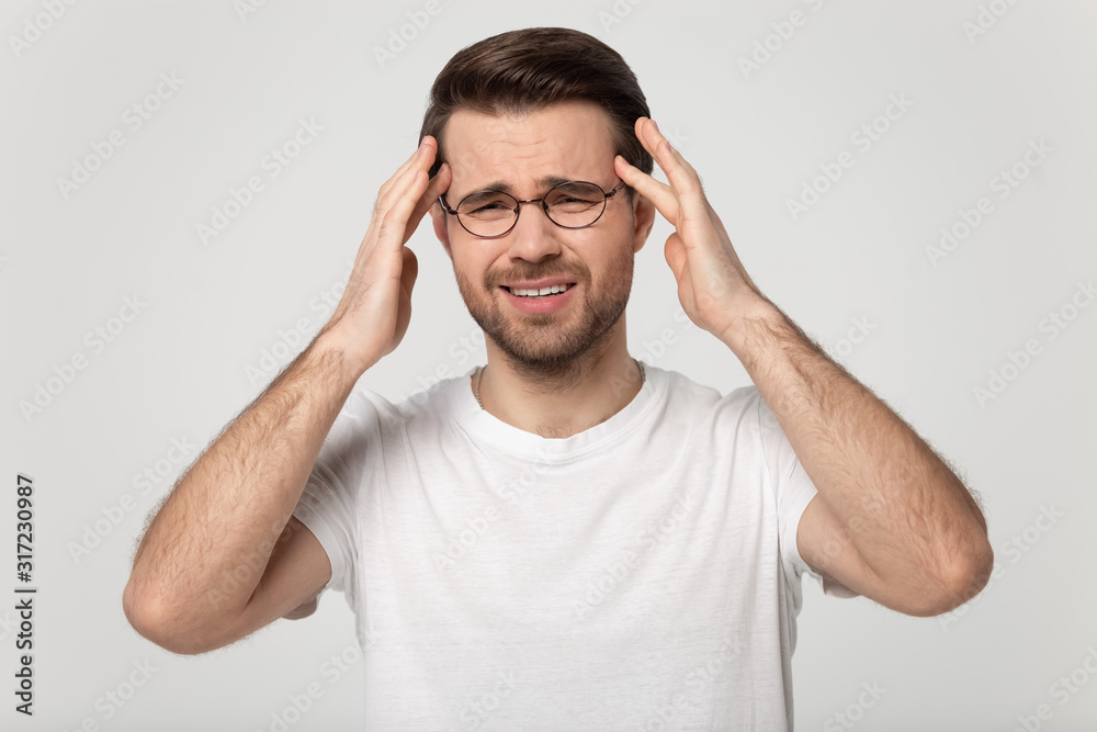 Tired millennial man massaging temples, suffering from sudden headache.
