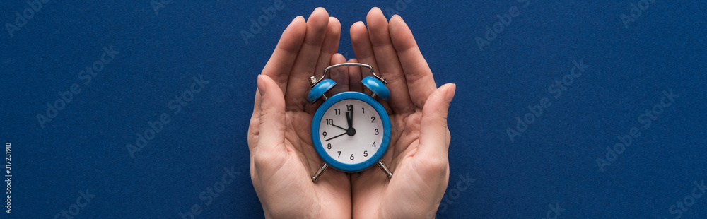 cropped view of woman holding alarm clock on blue background, panoramic shot cropped view of woman holding alarm clock on blue background, panoramic shot