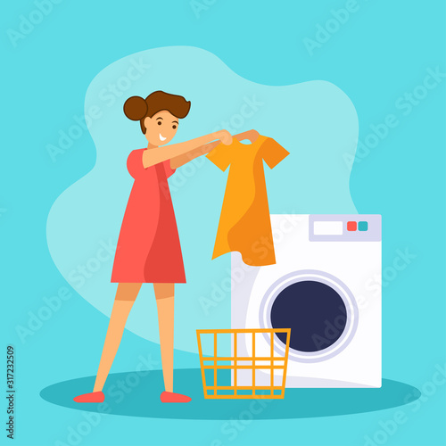 Young girl makes laundry at home. She standing near wash machine and holding clean dress in hands.