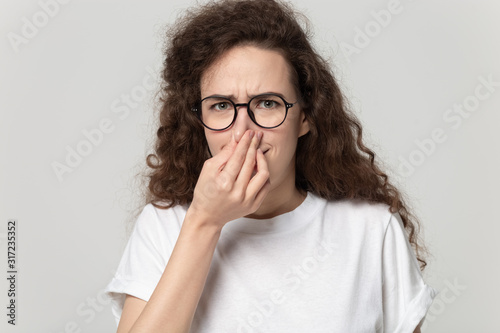 Young curly girl clenching nose, feeling unpleasant smell.