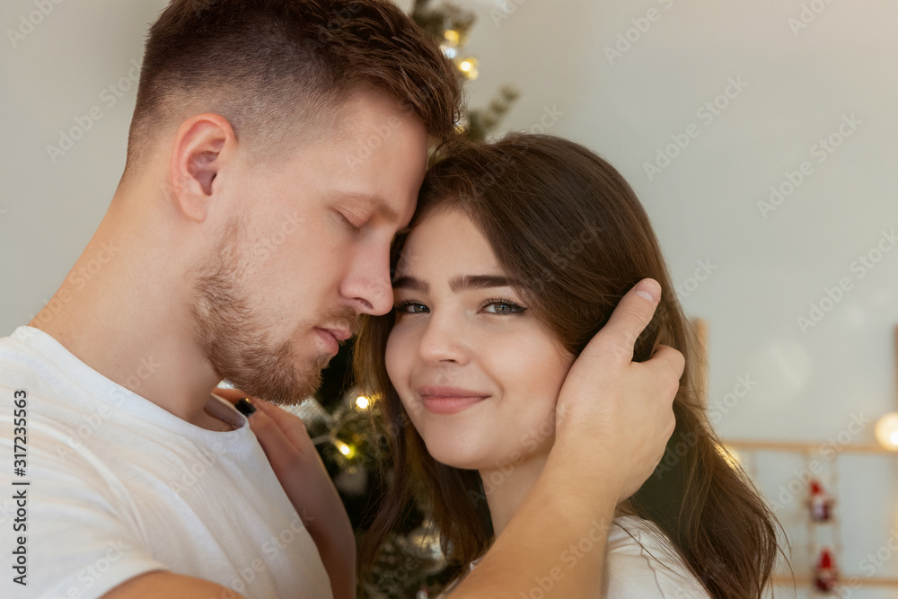 lovely couple husband hugging his beautiful wife standing near christmas tree both smiling in room decorated for celebrating new year festive mood love story lovely couple husband hugging his beautiful wife standing near christmas tree both smiling in room decorated for celebrating new year festive mood love story
