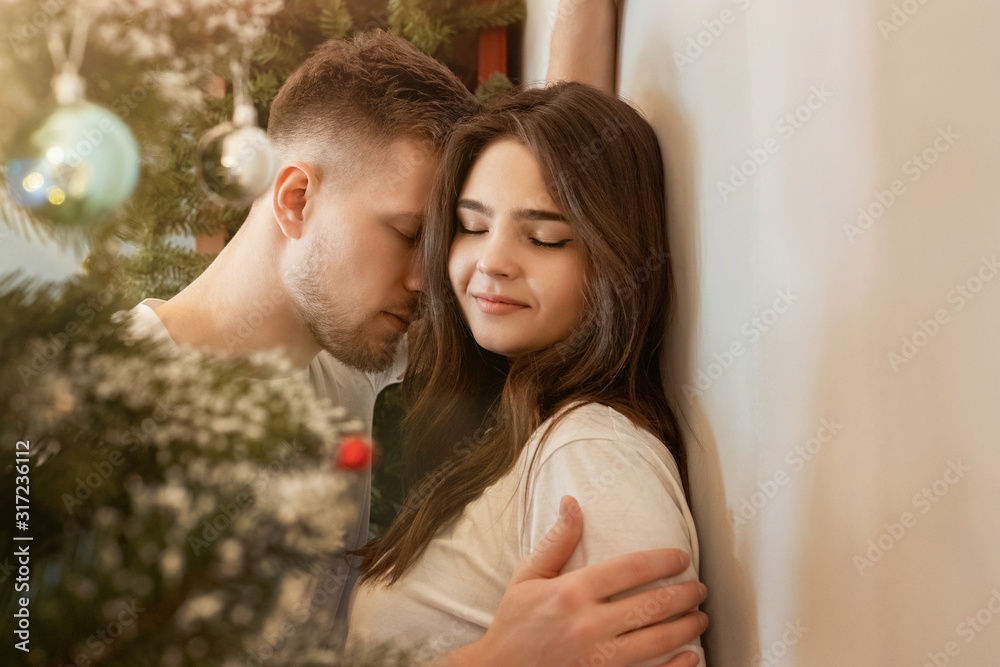 Fototapeta premium lovely couple husband hugging his beautiful wife with passion standing in room decorated for celebrating new year festive mood love story