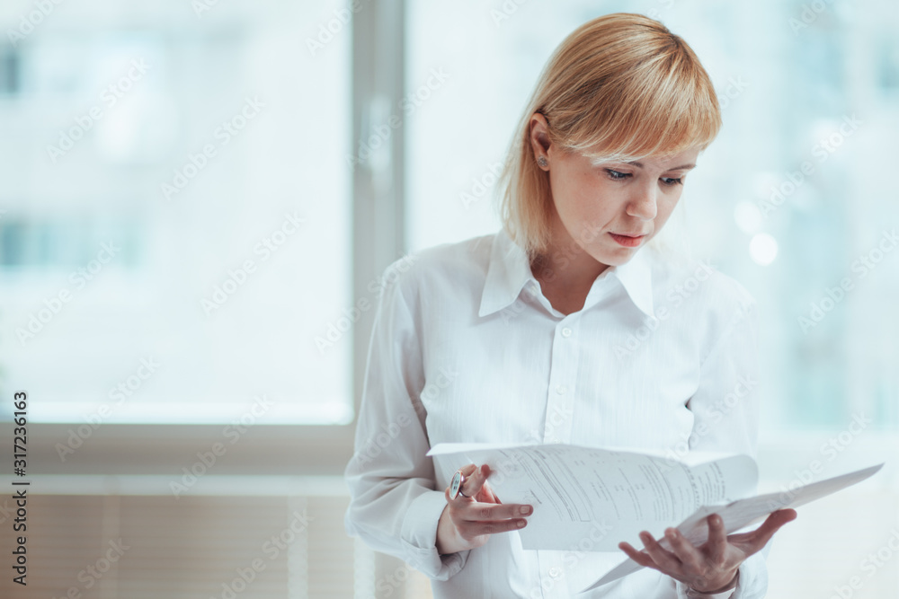 Woman in office, holding and reading documents - obrazy, fototapety, plakaty 