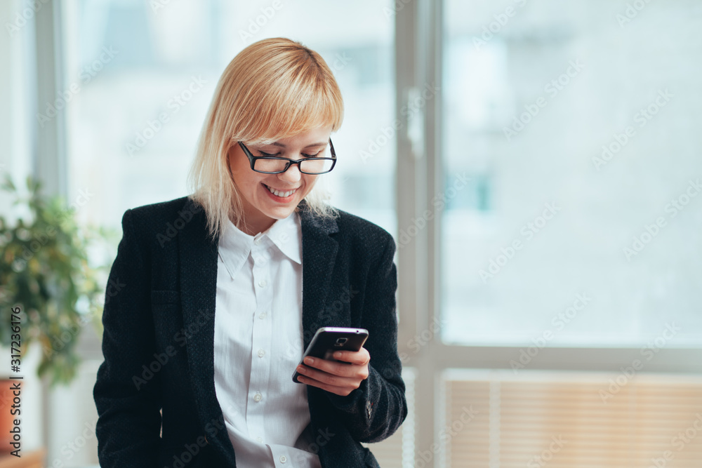 Woman in office smiling and looking at smartphone