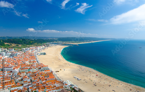 Portugal, panoramic view of Nazare in summer, mountain landscape with dense greenery in the background, Nazare coastline with white sand and blue azure water of the Atlantic Ocean, harbor Nazare