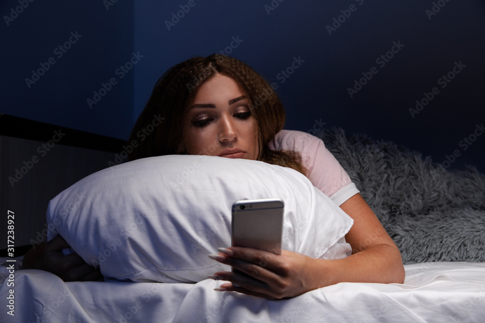 Tired internet addict young woman using phone in the dark room at home Tired internet addict young woman using phone in the dark room at home