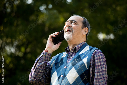 Happy senior man using phone at park