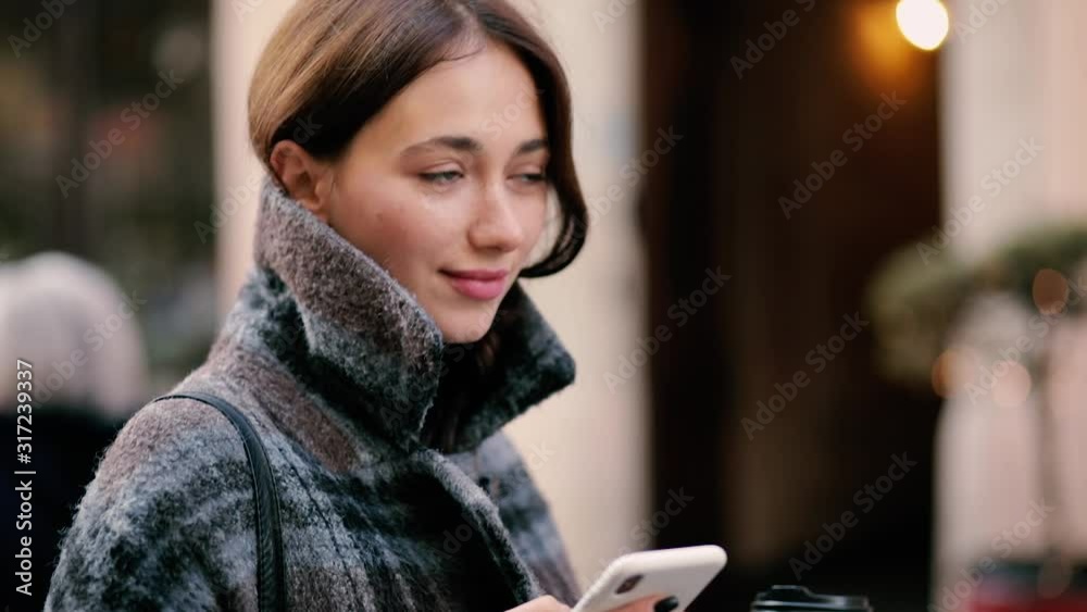 Young woman walking in the city center, using smartphone and drinking coffee. Communication, online shopping, social network concept Young woman walking in the city center, using smartphone and drinking coffee. Communication, online shopping, social network concept