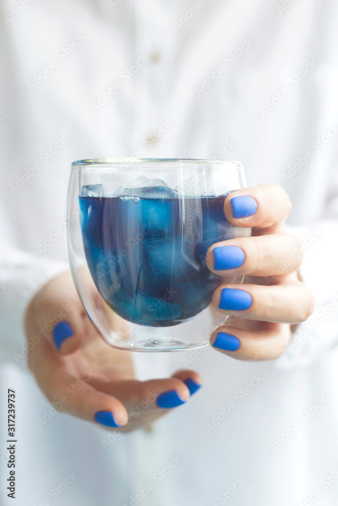 Blue matcha cold drink with ice in a glass beaker in the hands of a woman with blue manicure. Color of the year 2020 trend Blue matcha cold drink with ice in a glass beaker in the hands of a woman with blue manicure. Color of the year 2020 trend