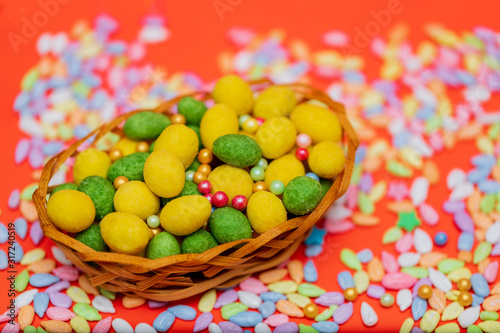 Easter composition, green and yellow dragee in a basket on a red background. Egg, nuts in the glaze, sunflower seeds in colored glaze. Flat lay.