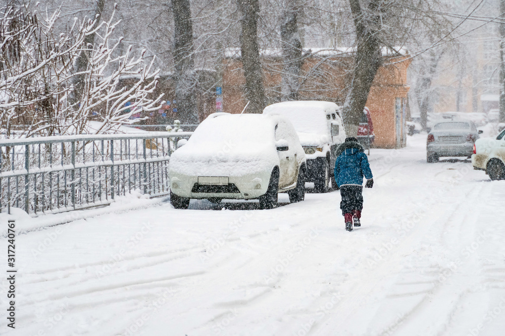 Fototapeta premium child walking in the snow next to parked cars