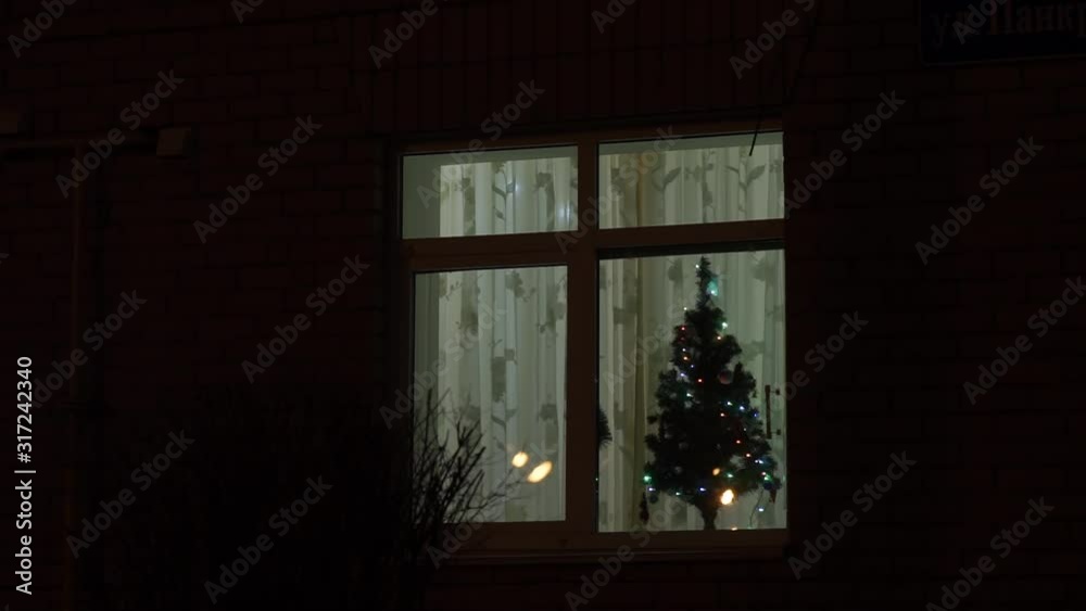 Christmas tree decorated with sparkling garlands in the window of the house Christmas tree decorated with sparkling garlands in the window of the house