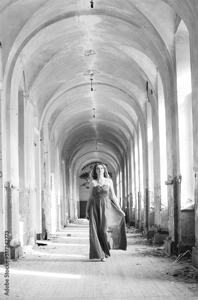 Young beautiful short hair blonde woman in black climbing the stairs, black and white photo. Side view of elegant romantic mysterious lady with movie star look in interior with bricks walls