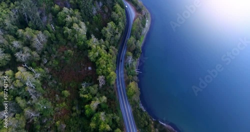 Car driving on a scenic windy road or highway along the lake or a river and forest in the evening (dusk). Aerial top view