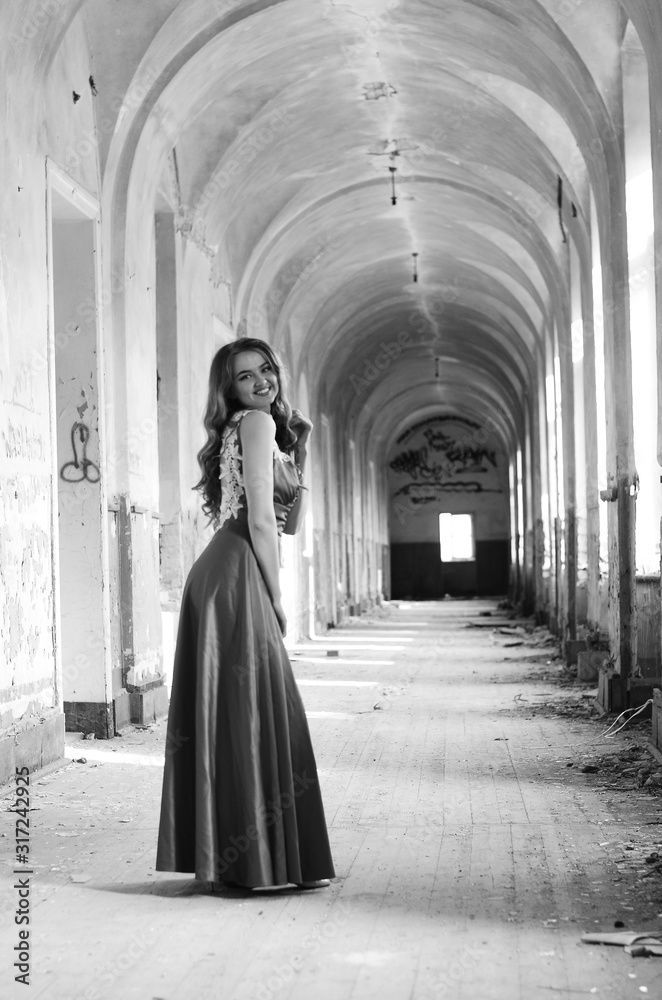 Naklejka premium Young beautiful short hair blonde woman in black climbing the stairs, black and white photo. Side view of elegant romantic mysterious lady with movie star look in interior with bricks walls