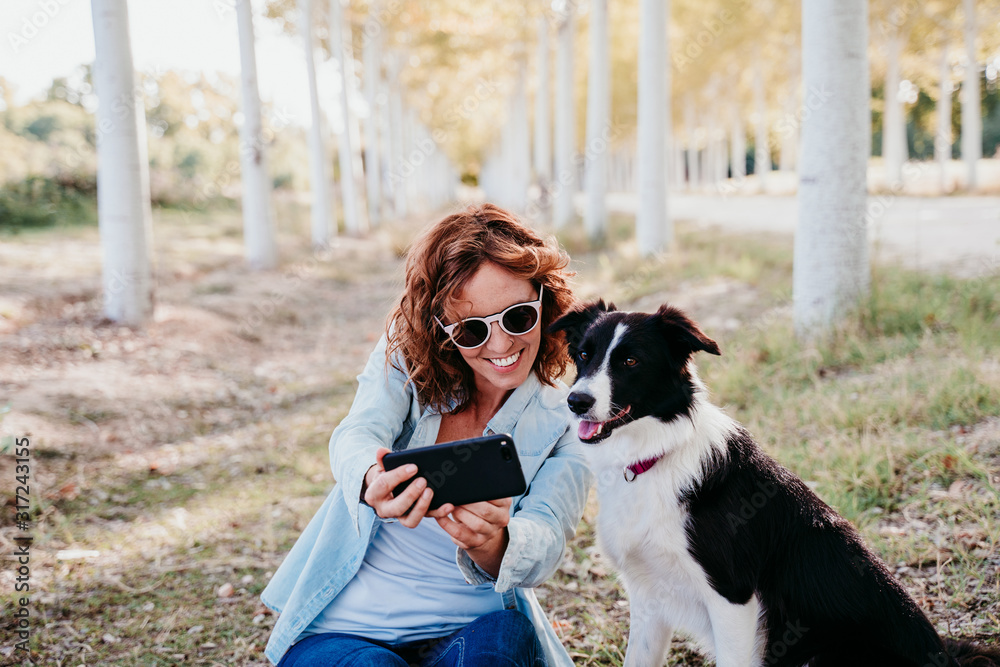 woman and beautiful border collie dog sitting in a path of trees outdoors. woman taking a selfie with mobile phone woman and beautiful border collie dog sitting in a path of trees outdoors. woman taking a selfie with mobile phone