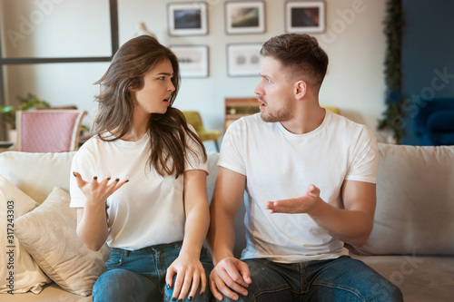 Wall Mural young couple man and woman sitting on the sofa both looking irritated, grimacing