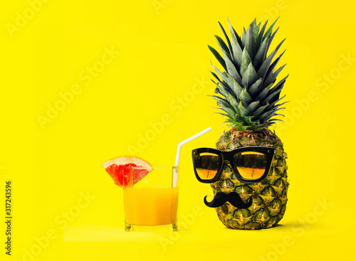 Two Fun Fashion pineapples with sunglasses and a mustache with fresh tropical smoothie with fruits on a yellow background. Husband and wife. Boy and girl.