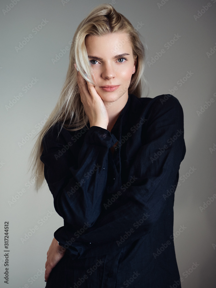 Fototapeta premium Young adorable blonde woman in black t-shirt dress posing next to window looking emotive and thoughtful