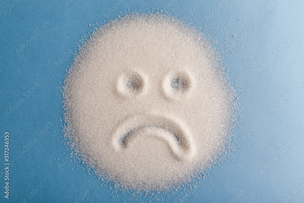 Salt scattered on black surface. Drawn sad face. Concept- diet, harm to health from excessive consumption of salt and sugar