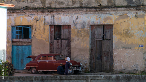 Photography two cuban men repairing a cuban classic car in front of an old house