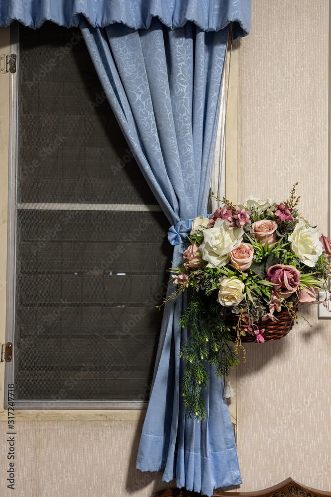 A bouquet of flowers in a basket hung with curtains by the window.
