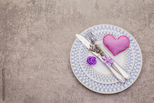 Romantic table setting on light stone concrete background. Valentine's day or Wedding card template. Lilac felt heart, lavender, rose flower, cutlery