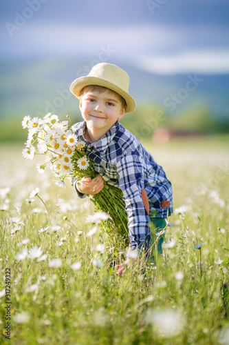 A boy in a hat in a meadow with green grass collects wildflowers.