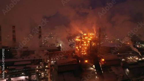 Top view of metallurgical plant blast furnace at night with smokestacks and fire blazing out of the pipe. Industrial panoramic landmark with blast furnance of metallurgical production photo