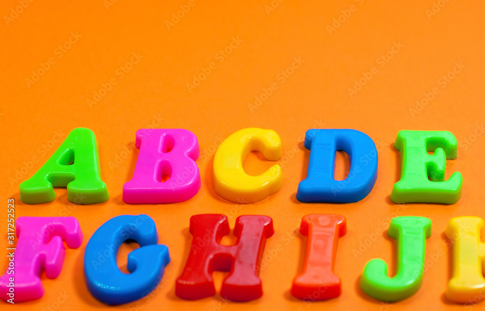 Naklejka premium Plastic color letters on a bright contrasting orange background, multicolored alphabet with copy space