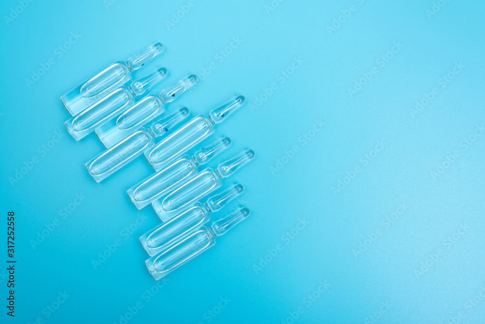 Ampules with a transparent preparation on a blue light background. Concept: drugs, injections, treatment, medicine. Ampules with a transparent preparation on a blue light background. Concept: drugs, injections, treatment, medicine.
