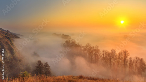 Autumn sunrise landscape - view of a river valley covered with fog in the light of the sunrays, the northeast of Ukraine