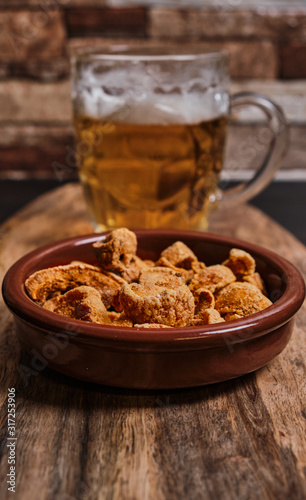 Torreznos and a beer jar on a wooden table. Spanish typical food, fried pork bacon. Appetizer.