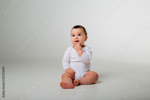 baby boy 9 months in a white bodysuit sitting on a white background, space for text