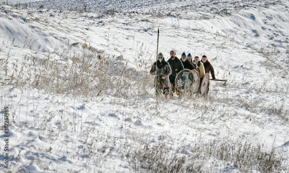 Group of Vikings with shields and swords going forward on the winter meadow. Male, leader. Group of Vikings with shields and swords going forward on the winter meadow. Male, leader.