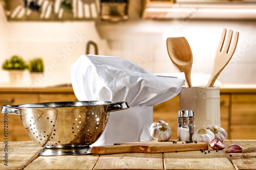 Brown kitchen furniture with empty space on table.Copsy space and kitchen board.White cook hat and few kitchen utensils.Free space for your product and morning time.  photo